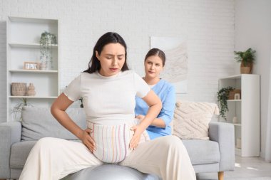 Eşarplı genç Doula hamile kadına evde spor salonunda masaj yapıyor.