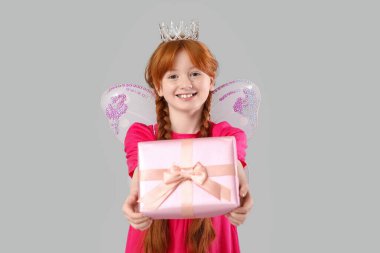 Gri arka planda hediye kutusuyla peri gibi giyinmiş tatlı kızıl kız.