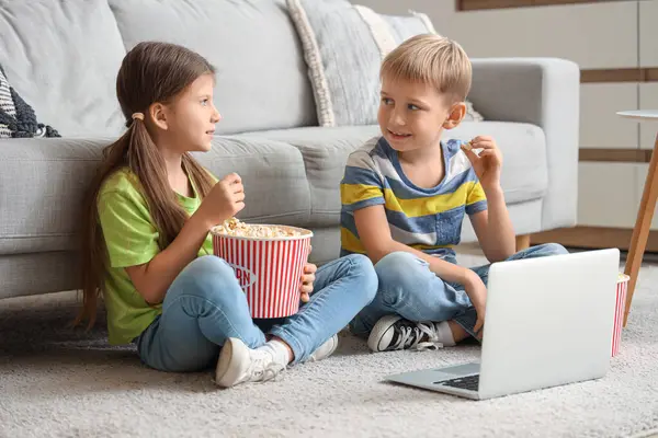 Patlamış mısırlı küçük çocuklar evde dizüstü bilgisayardan film izliyorlar.