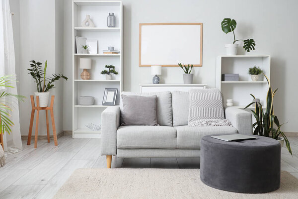 Interior of living room with grey sofa, pouf and shelf units