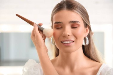 Profesyonel makyöz stüdyoda genç bir kadına yüz kızartıcı sürüyor.