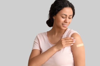 Hafif arka planda aşıdan sonra tıbbî yaması olan genç Afro-Amerikalı kadın, yakın plan.