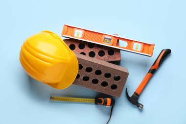 Mavi arkaplanda sert şapka, tuğla ve inşaat araçları