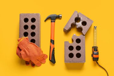 Sarı arka planda tuğlalar, eldivenler ve inşaat araçları