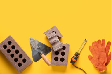 Sarı arka planda tuğlalar, eldivenler ve inşaat araçları