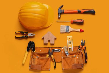 Ahşap ev modeli, turuncu arka planda baret ve inşaat araçları