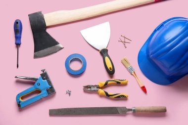 Pembe arka planda sert şapka, balta ve inşaat araçları