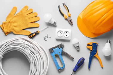 Gri arkaplanda sert şapka, kablolar, ampuller ve inşaat araçları