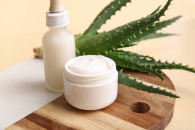Bir şişe kozmetik yağı ve bej arka planda aloe vera yapraklı krema.