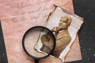 Yaşlı bir adamın eski fotoğrafı ve koyu arkaplanda büyüteç var.