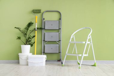 Boya silindirli merdivenler, kovalar ve yeşil duvarın yanındaki bitkiler.