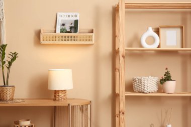 Lambalı ahşap masa ve odada bej duvarın yanındaki süslemeli raf.