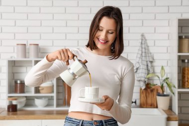 Geyser kahve makinesinden mutfakta fincana taze espresso döken güzel genç bir kadın.