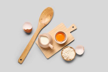 Süt sürahisi, çiğ tavuk yumurtası, un ve gri arka planda ahşap kaşık kompozisyonu