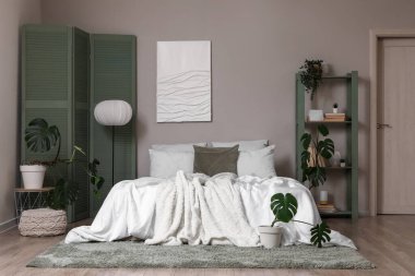 Yatak odasının içinde yeşil ekran, raf ünitesi ve bitkiler var.