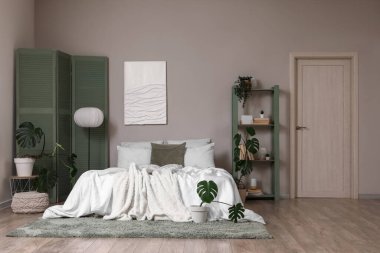 Yatak odasının içinde yeşil ekran, raf ünitesi ve bitkiler var.