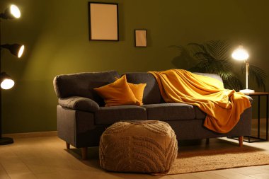 Gece oturma odasının içinde, kanepe, puf ve yeşil duvarın yanında parlayan lambalar.