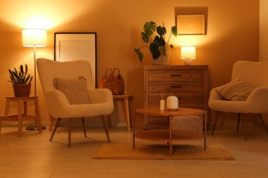 Gece oturma odasının içinde koltuklar, tuvalet, sehpa ve sarı duvarın yanında parlayan lambalar.