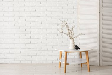 Katlanan ekran ve çiçek açan ağaç dalları beyaz tuğla duvarın yanındaki sehpanın üzerinde.