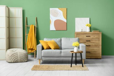 Soyunma odası, kahve masası ve yeşil duvarlı narsist çiçekli rahat bir kanepe.