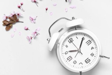 Çalar saat ve gri arka planda çiçekler. Bahar geldi.