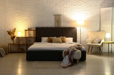 Yumuşak gri yataklı, rahat koltuklu ve geceleri parlayan lambalı bir yatak odası.