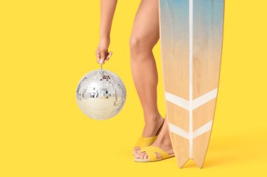 Sarı arka planda sörf tahtası ve disko topu olan güzel bir kadın.