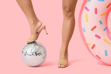 Şişme yüzüklü kadın bacakları ve pembe arka planda disko topu.