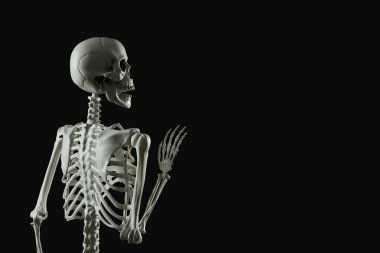Korkunç insan iskeleti siyah arka planda el sallıyor.