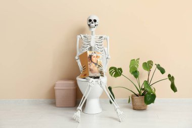 Tuvaletteki klozetin üzerinde dergi olan insan iskeleti.