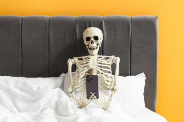 Yatağında cep telefonu olan insan iskeleti.