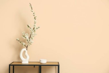 Bej duvarın yanındaki masada çiçek açan ağaç dalları olan vazo.