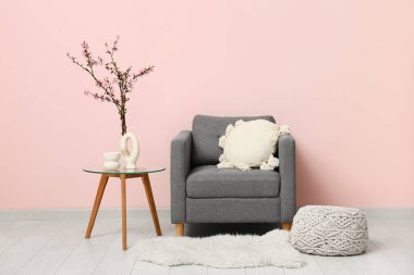 Gri koltuğu ve kahve masasının üzerinde çiçek açan ağaç dalları olan şık bir oturma odası.