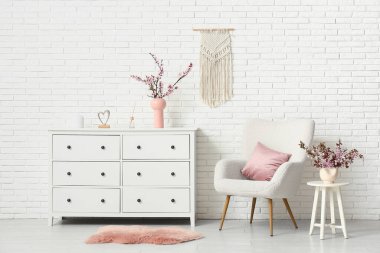 Beyaz koltuklu şık bir oturma odası, şifoniyerde çiçek açan ağaç dalları ve kahve masası.