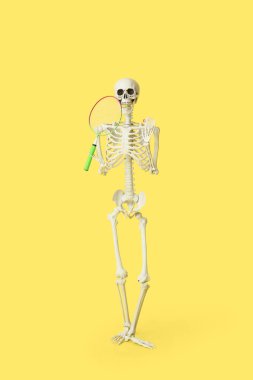 Badminton topu ve sarı arka planda raketi olan komik bir insan iskeleti.