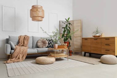 Oturma odasının içinde gri kanepe, masa ve vazoda çiçek açan dallar.