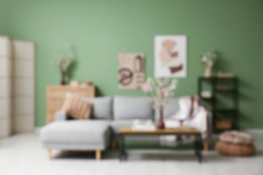 Kahve masası, şifonyer ve oturma odasındaki yeşil duvarın yakınındaki çiçek açan dalların olduğu koltuğun bulanık görüntüsü.