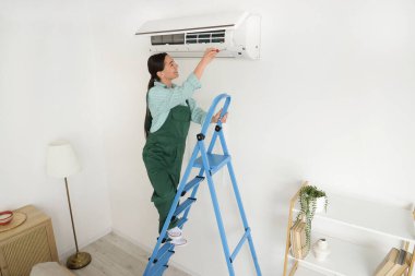 Odasında klima tamir eden tornavidalı bir kadın işçi.