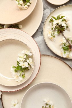 Gri arkaplanda çiçek açan dalları olan temiz bej plakalar, yakın plan.