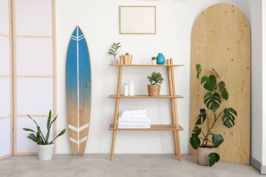 Raflarla, ev bitkileriyle ve sörf tahtasıyla aydınlık banyonun içinde.