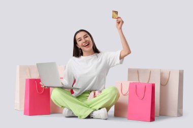 Bilgisayarlı ve kredi kartlı mutlu genç bir kadın beyaz arka planda online alışveriş yapıyor.