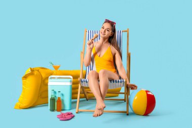 Dondurmalı güzel kadın güvertede oturuyor ve mavi arka planda plaj aksesuarları var.