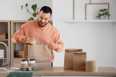 Genç adam mutfaktaki kese kağıdından konteynır alıyor. Yemek dağıtım servisi.