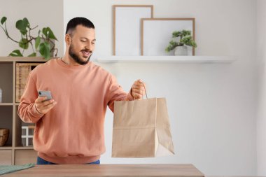Mutfakta kese kağıdı ve cep telefonu olan genç bir adam. Yemek dağıtım servisi.