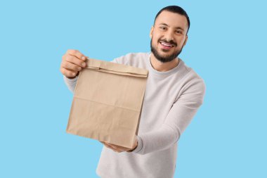 Mavi arka planda kese kağıdı olan genç bir adam. Yemek dağıtım servisi.
