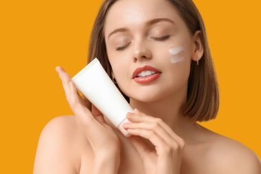 Yüzünde güneş kremi ve sarı arka planda tüp olan güzel genç bir kadın.