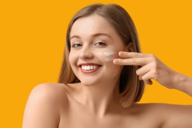Sarı arka planda güneş kremi sürmüş güzel genç bir kadın.