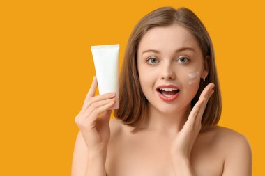 Yüzünde güneş kremi ve sarı arka planda tüp olan güzel genç bir kadın.