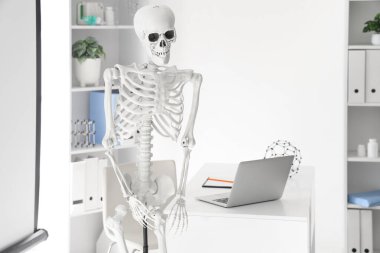 Işık hastanesi konferans salonunun içinde insan iskeleti modeli, masa ve projektör ekranında modern dizüstü bilgisayar, yakın çekim
