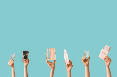 Mavi arka planda sörf tahtası, kamera ve pasaport olan mini güverte sandalyeleri tutan kadın eller.